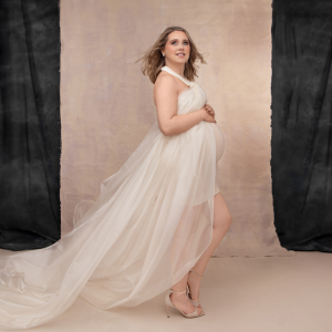 Lady stands and holds her bump in a beautiful white flowing dress