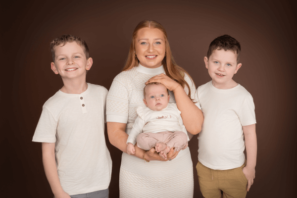Family photo of siblings holding a newborn.