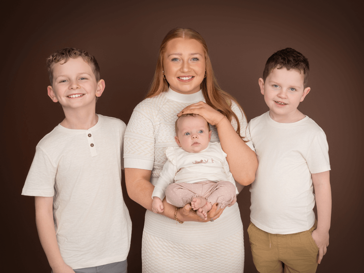 Newborn held by a sibling, surrounded by two others, photographed by Shauna at Morning Star Photography